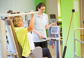 Eine Angestellte der Rehaklinik Sonnhalde betreut eine Patientin bei einer Übung an einem Fitnessgerät.