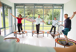 Patientinnen und Patienten machen Gymnastikübungen auf kleinen Trampolinen.