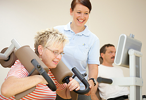 Eine Angestellte der Rehaklinik Sonnhalde hilft einer Patientin bei einer Übung an einem Fitnessgerät.